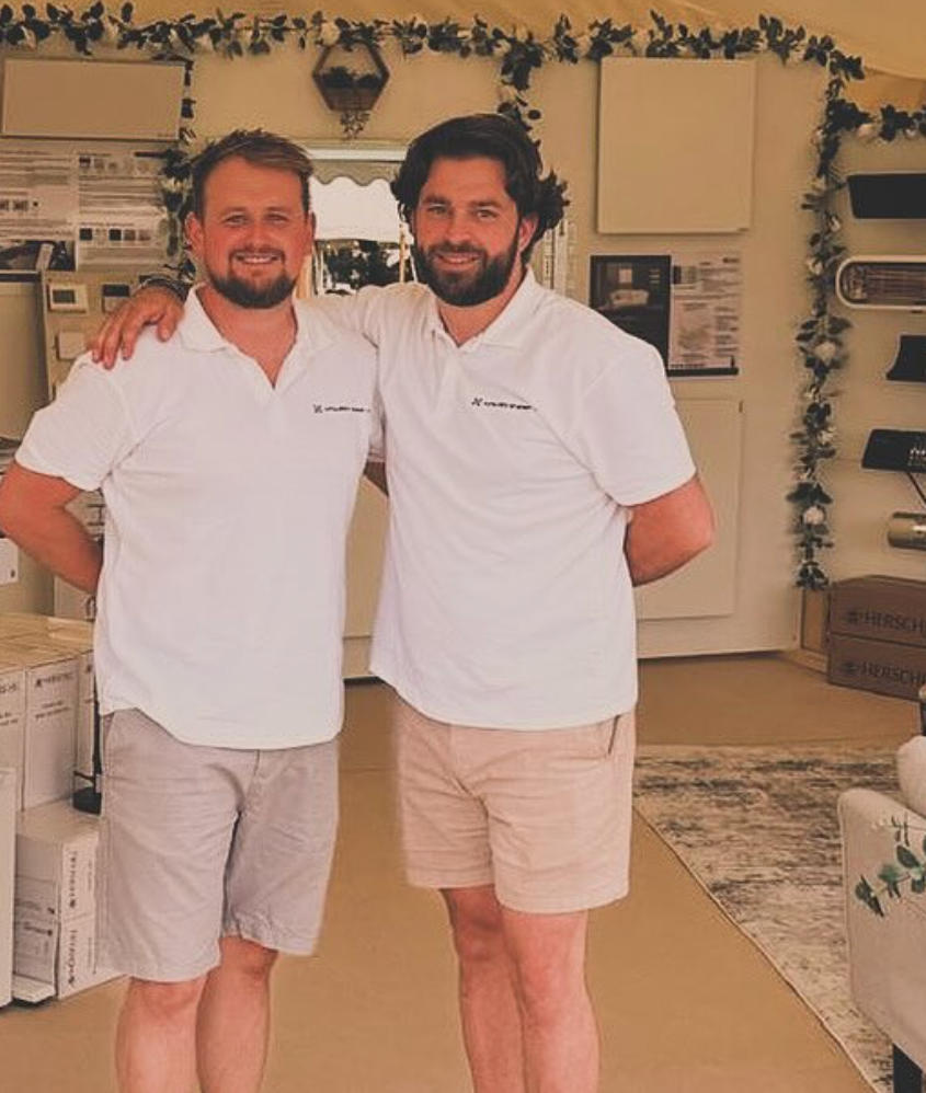 Two men in white polo shirts standing in a room with decorative elements.